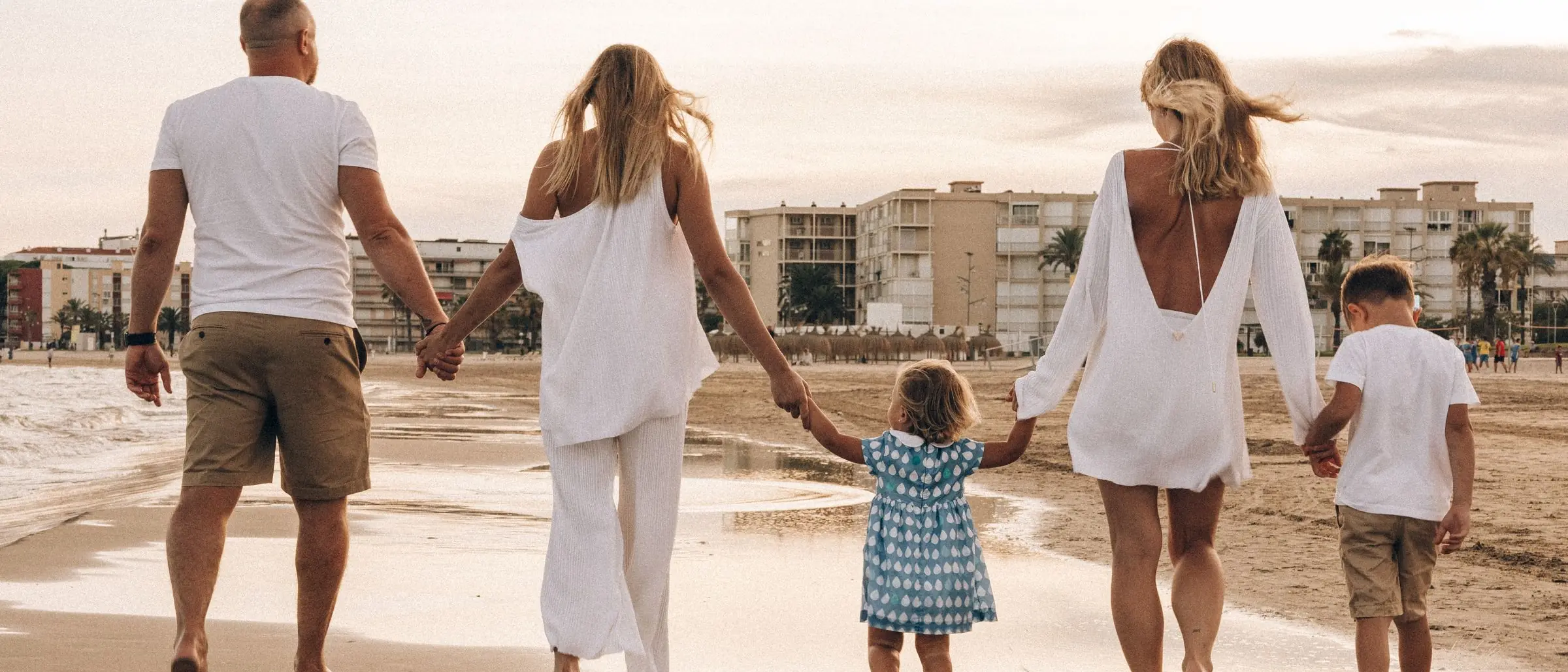 Familia caminando de la mano por la playa al atardecer